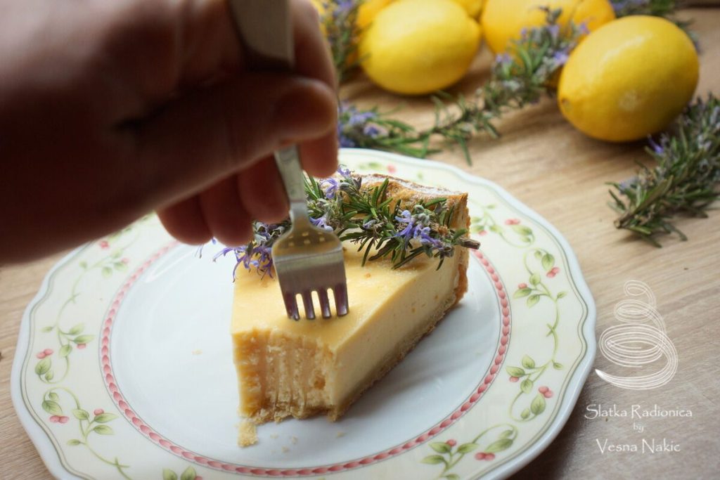 Torta od sira poslužena na tanjuru, dekorirana cvijetom ružmarina i limunom