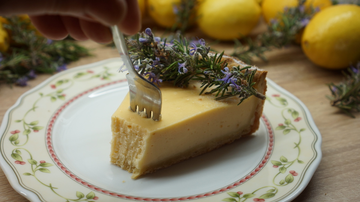 Torta od sira poslužena na tanjuru, dekorirana cvijetom ružmarina i limunom