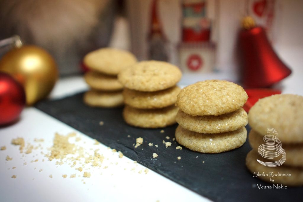 đumbir keksi, zlatne boje, složeni u nekoliko redova na crnoj kamenoj podlozi uz dodatak božićnih dekoracija zlatne i crvene boje